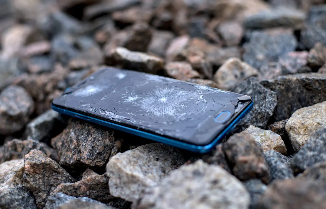 Cracked smartphone on rough, rocky surface.